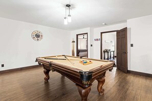 A pool table in a room with a wooden floor, white walls, and a ceiling fan. - Maplecrest Retreat | Firepit • Hot Tub • Game Room (Sevierville)