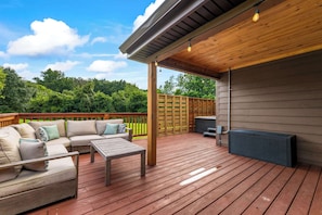 A covered outdoor deck with a sofa, table, and grill area. - Maplecrest Retreat | Firepit • Hot Tub • Game Room (Sevierville)