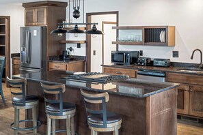 Eine moderne Küche mit einer zentralen Kochinsel, Barhocker, einem Kühlschrank, einer Mikrowelle, einem Toaster und einem Geschirrspüler.