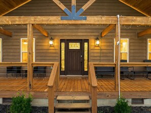 A wooden building with a porch, a dark entrance door, and two windows with lights. - Maplecrest Retreat | Firepit • Hot Tub • Game Room (Sevierville)