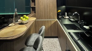 A modern kitchen with a built-in oven, a sink, and a countertop with a bowl of fruit and glasses.