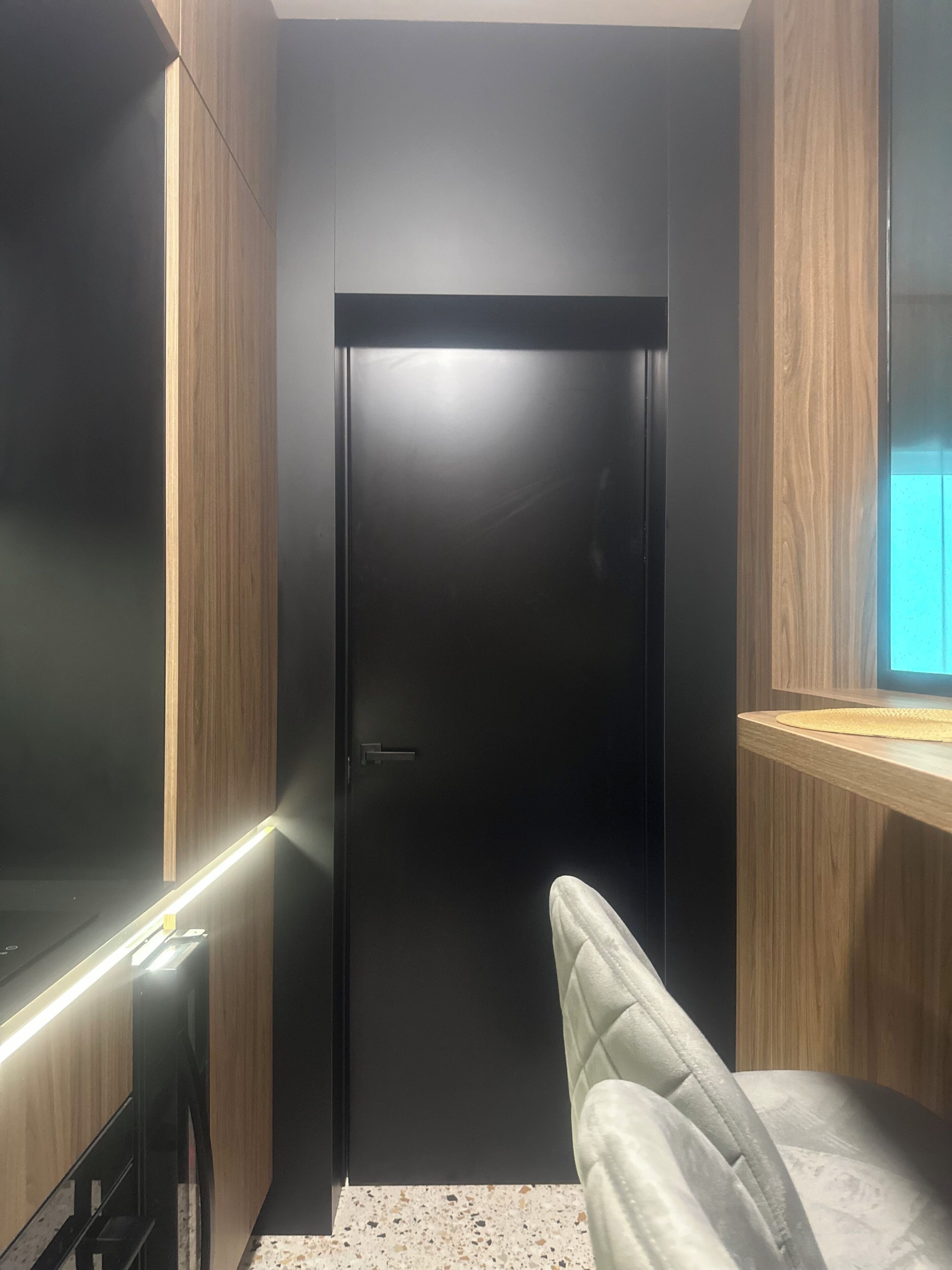 A modern interior with a dark door, wooden paneling, and a seating area with a light-colored cushion.