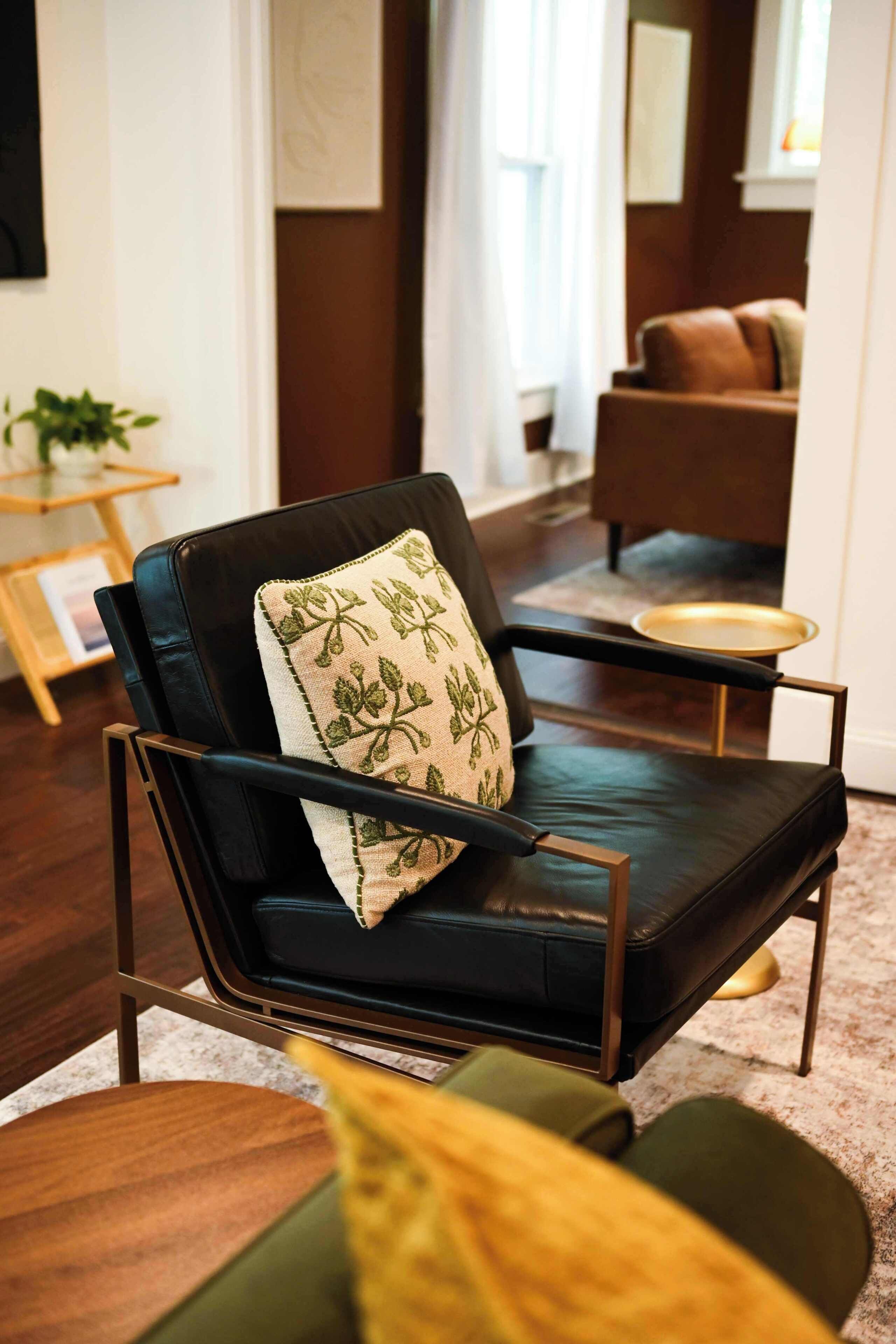 Un salon moderne avec un canapé en cuir noir, un coussin décoratif à motifs et une petite table d’appoint sur laquelle est posée une plante.