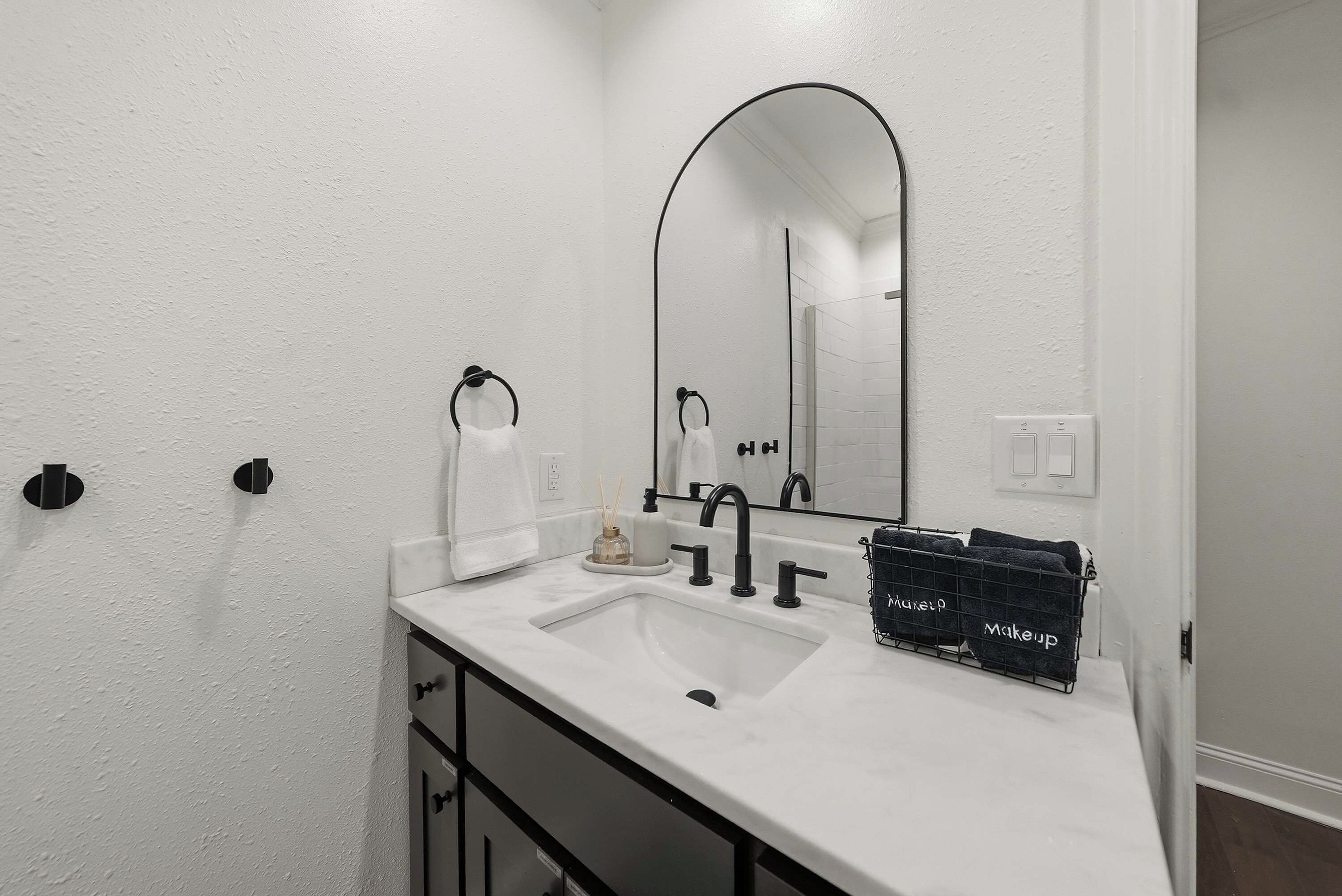 Un bagno con un lavandino bianco, un porta asciugamani nero e uno specchio.