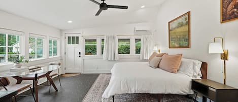 Une chambre d’hôtel avec un lit, un bureau, une chaise, un ventilateur de plafond et un tableau au mur.