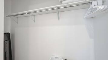 A white closet with a metal rod for hanging clothes and a white plastic basket.