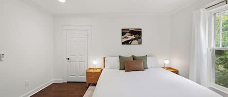 A bedroom with a bed, bedside tables, a ceiling fan, a door, and a window.