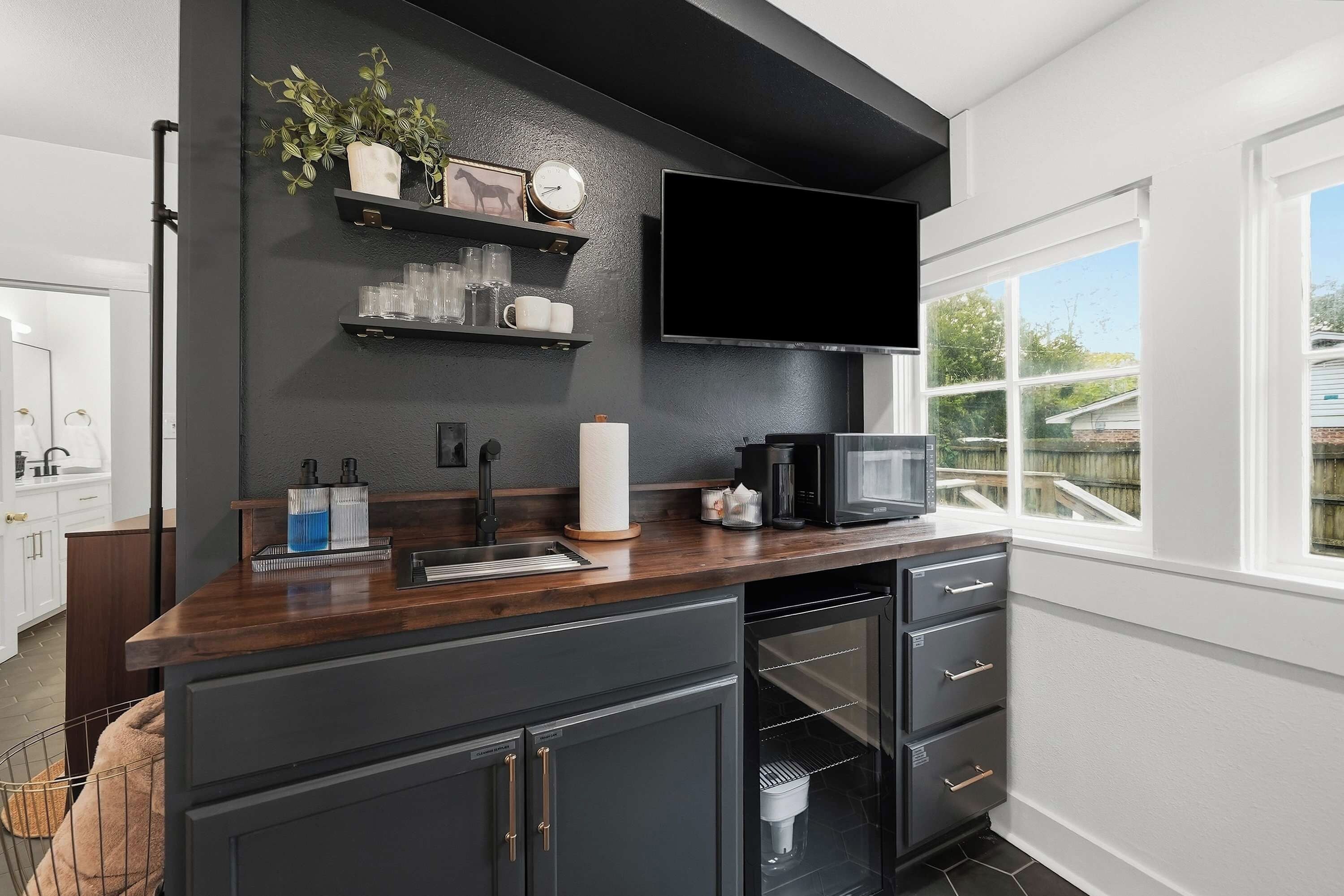 A modern kitchen with a dark countertop, black cabinets, a built-in microwave, and a window with a view of the outdoors.