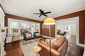 A spacious living room with a brown accent wall, a ceiling fan, a large floor lamp, and a leather sofa. - Caldwell House + Studio - Walk Downtown - 1 mi UCA (Conway)