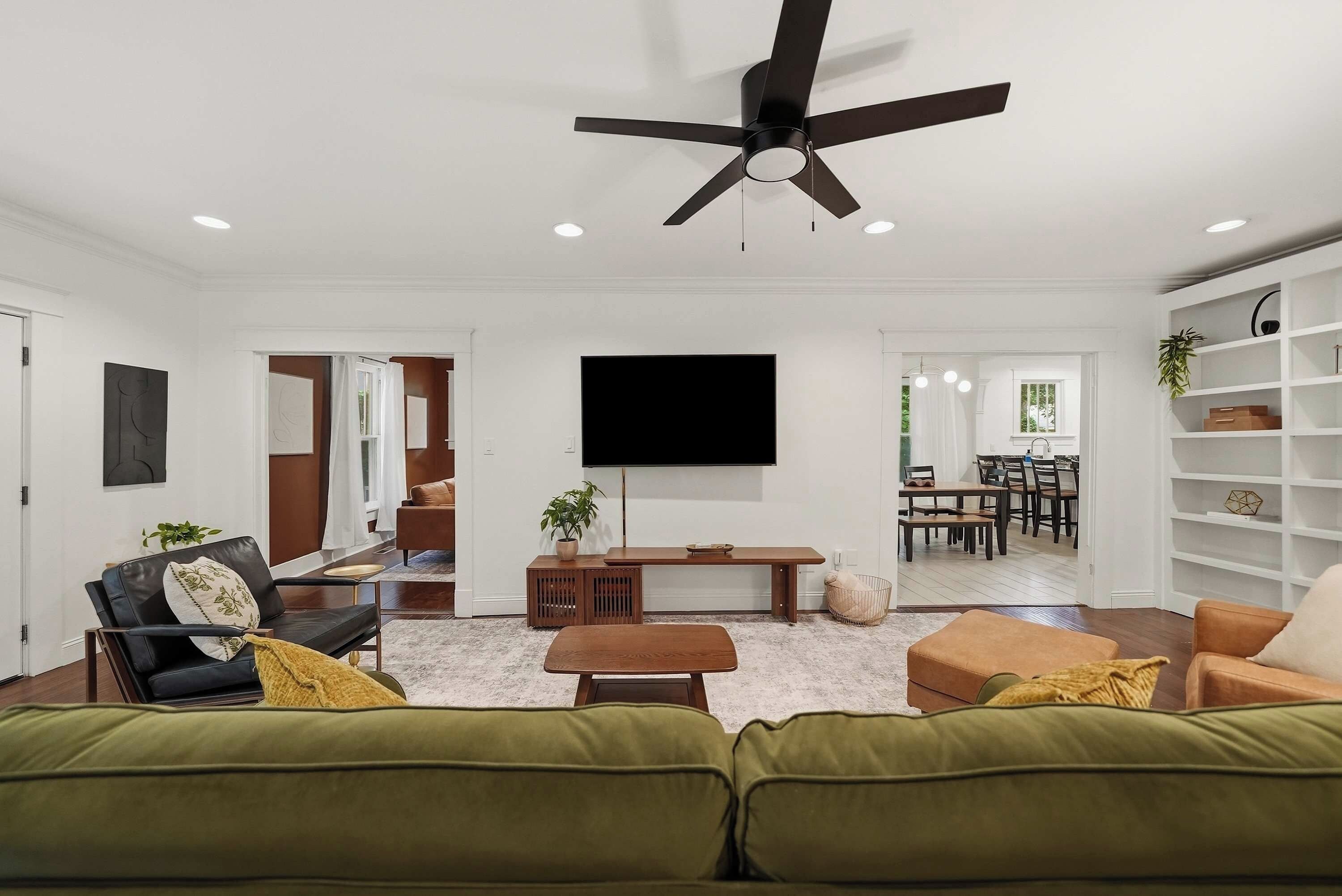 Una sala de estar moderna con ventilador de techo, televisor de pantalla plana, sofá, mesa de centro y una zona de comedor al fondo.