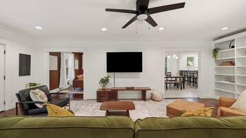 Una sala de estar moderna con ventilador de techo, televisor de pantalla plana, sofá, mesa de centro y una zona de comedor al fondo.