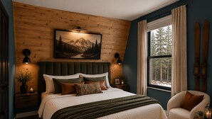 A bedroom with a large bed, a headboard, a nightstand, a bedside table, a window with curtains, and a view of trees. - Designer A-Frame, Hot Tub, Mountain Views, Game Room (Divide)