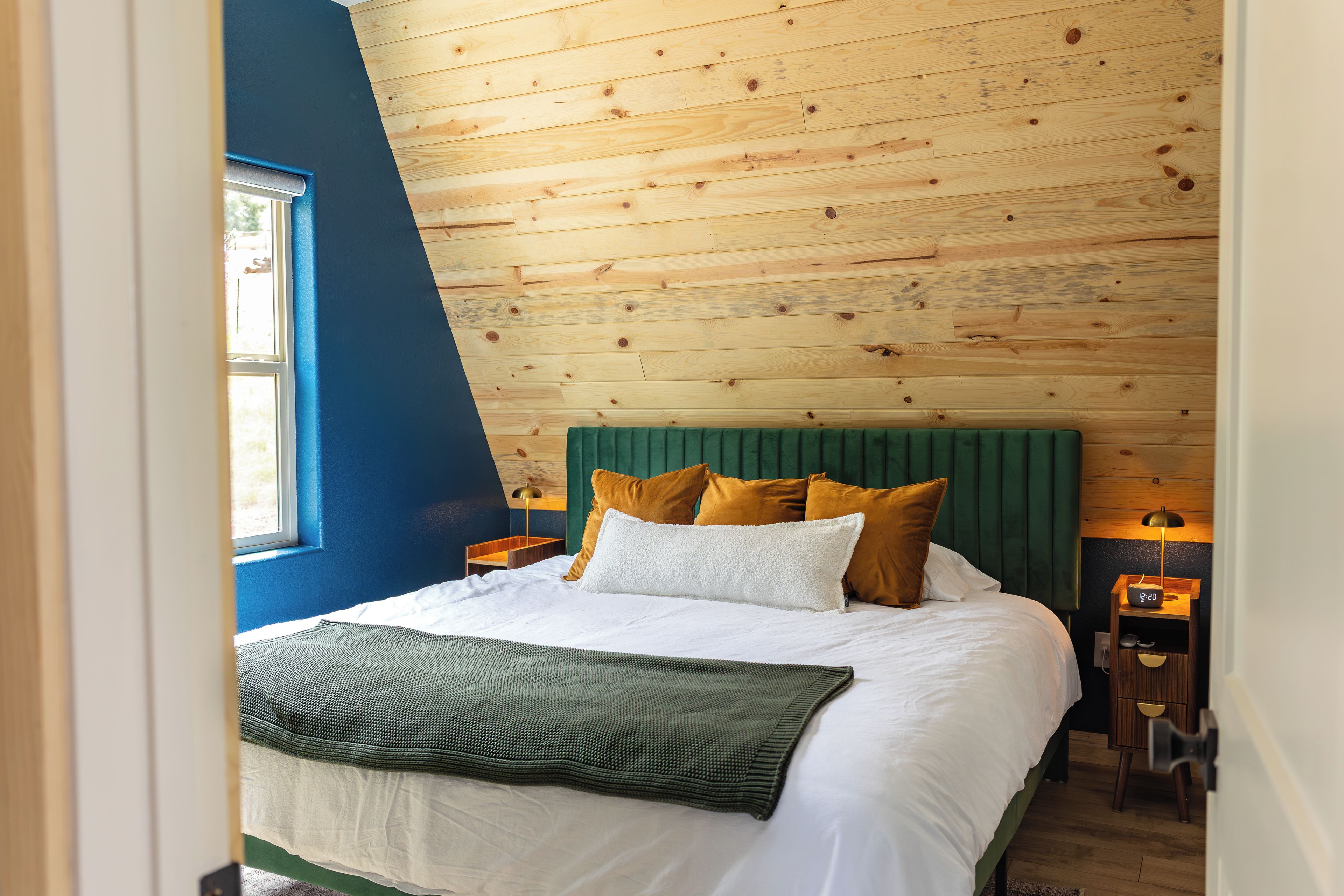 Une chambre avec un plafond en pente, un lit avec de nombreux oreillers, une table de chevet avec une lampe et une fenêtre.