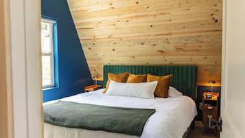 Une chambre avec un plafond en pente, un lit avec de nombreux oreillers, une table de chevet avec une lampe et une fenêtre.
