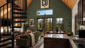 A spacious loft with a high ceiling, a spiral staircase, a large window, and a kitchen area. - Designer A-Frame, Hot Tub, Mountain Views, Game Room (Divide)