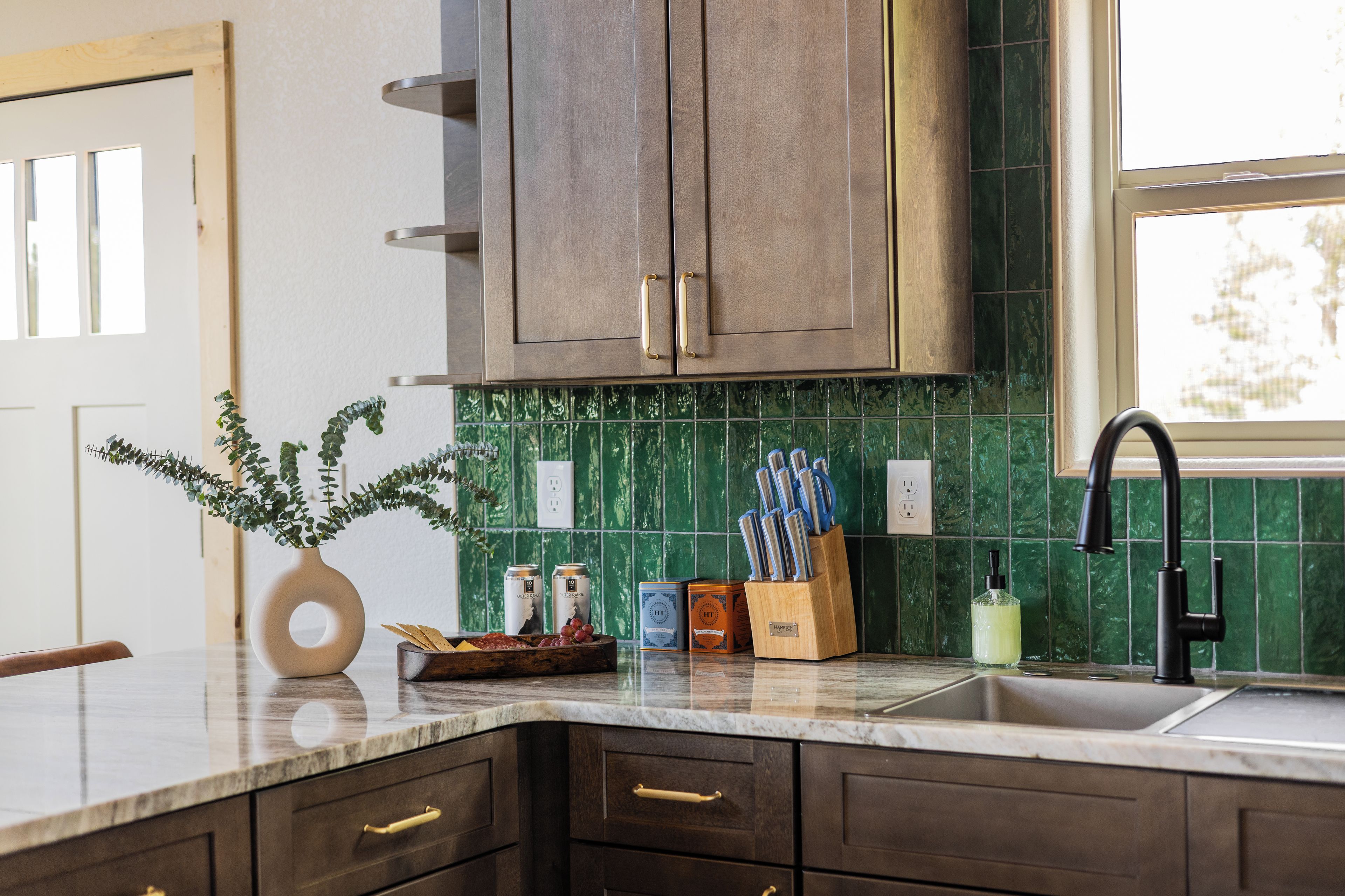 A kitchen with dark wooden cabinets, a green tiled backsplash, and a marble countertop.