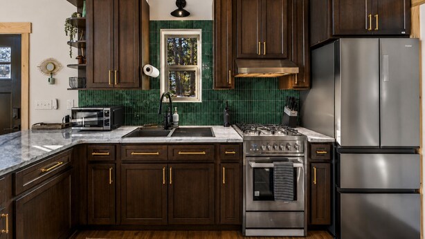 A kitchen with dark wooden cabinets, stainless steel appliances, and a green tiled backsplash. - Designer A-Frame, Hot Tub, Mountain Views, Game Room (Divide)