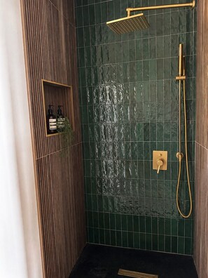 A bathroom with a shower, a wall-mounted shelf with toiletries, and a drain. - Designer A-Frame, Hot Tub, Mountain Views, Game Room (Divide)
