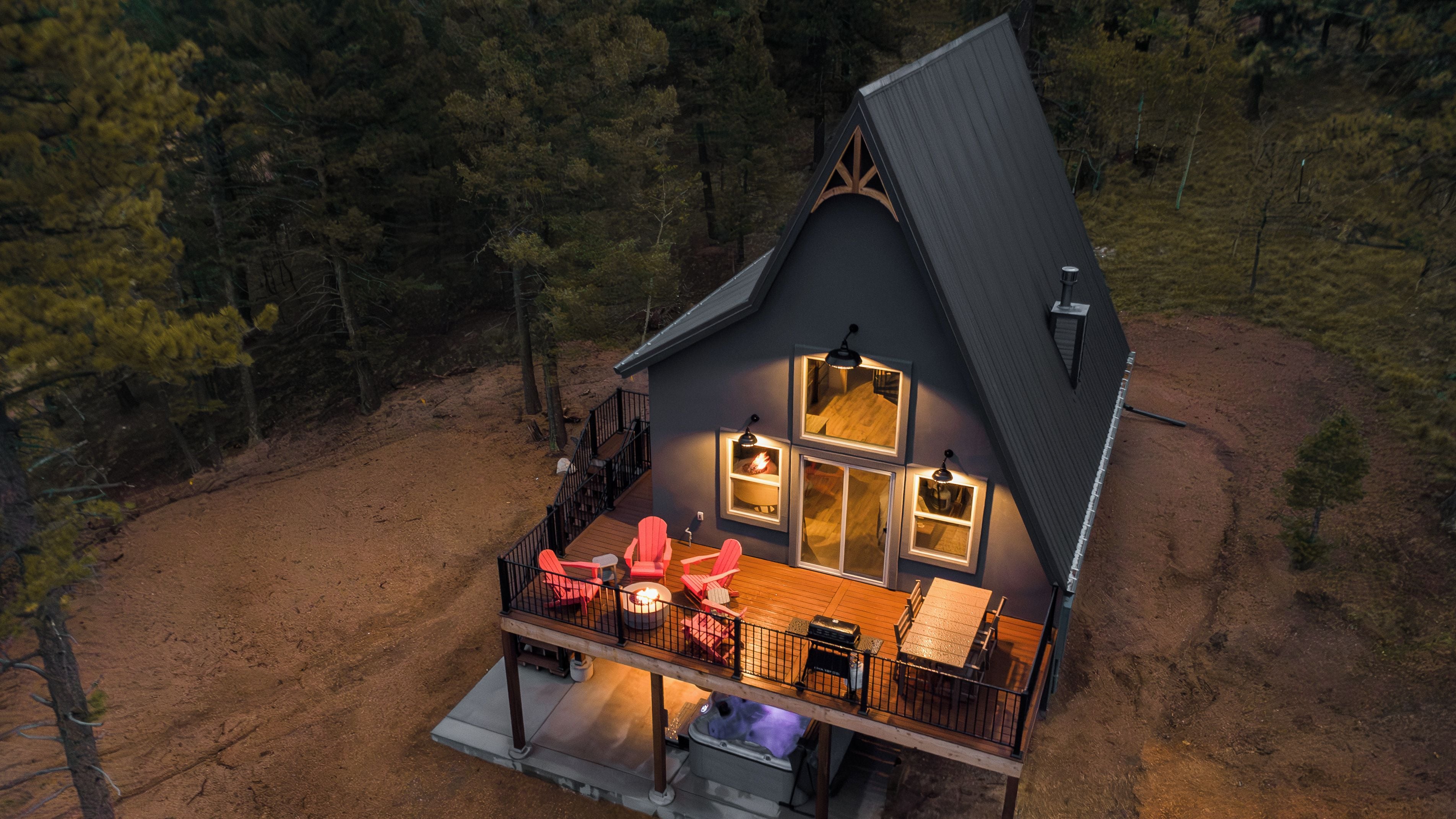 A cabin with a deck, outdoor seating, and a fireplace.