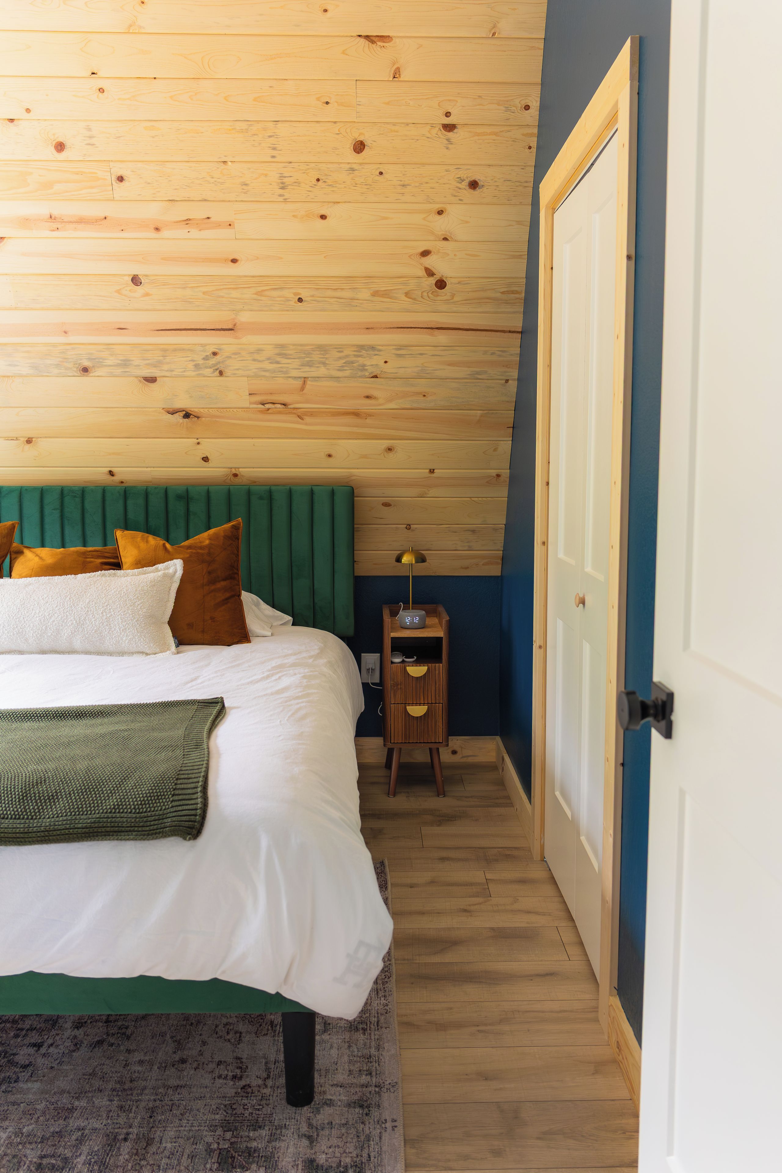 A bedroom with a wooden ceiling, a green upholstered headboard, a bed with white bedding, and a bedside table with a lamp.