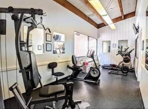 Ein Heimfitnessstudio mit Trainingsgeräten, darunter eine Hantelbank, ein Laufband und ein Ergometer.