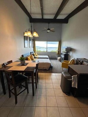 Ein Zimmer mit Essbereich, einer Couch, einem Fernseher und Blick ins Freie.