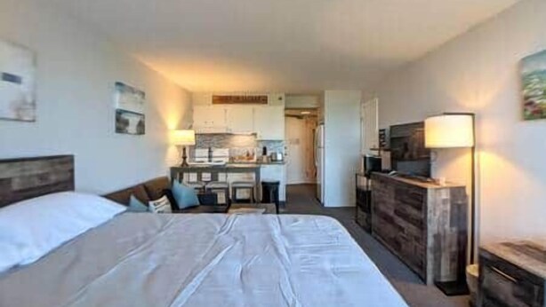 Quarto de hotel com cama, escrivaninha, cozinha compacta e televisão.