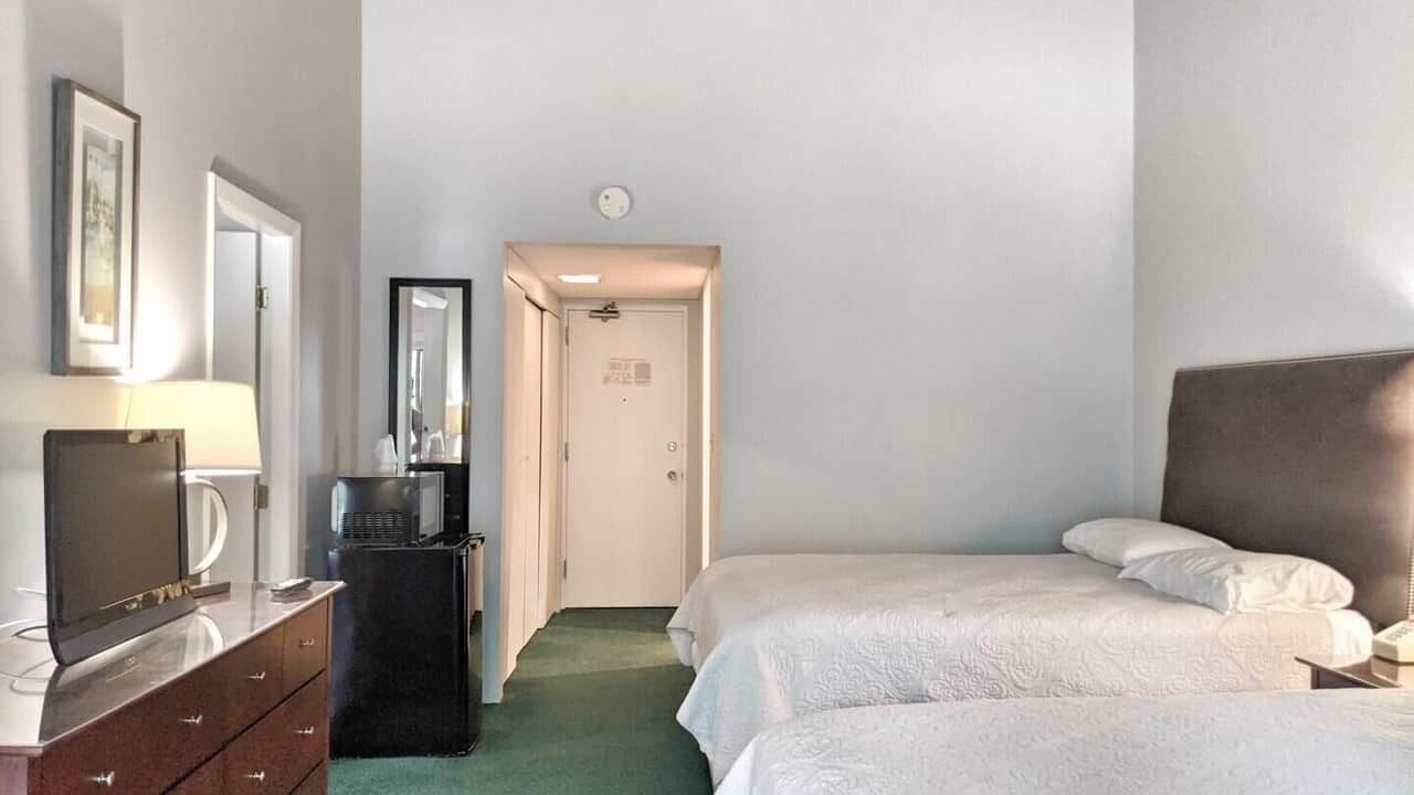Et hotelværelse med to senge, et skrivebord med et fladskærms-tv, en kommode, en mikrobølgeovn og en dør, der fører til et andet rum.
