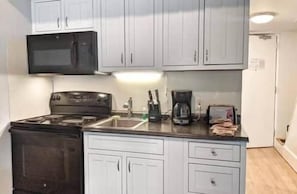 Una cocina compacta con armarios blancos, estufa, microondas, cafetera y tostadora.