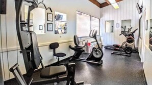 Een fitnessruimte met trainingsapparatuur, een loopband en een stoel.