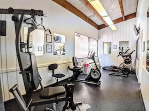 Ein Fitnessraum mit Trainingsgeräten, Laufband und Stuhl.