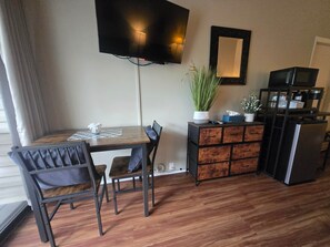 Eine moderne Küche mit Holztisch, Stühlen, Fernseher, Kühlschrank und einer Pflanze.