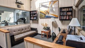 Ein gemütliches Wohnzimmer mit einer Couch, einem Couchtisch, einem Schreibtisch mit Computer und Bücherregalen.