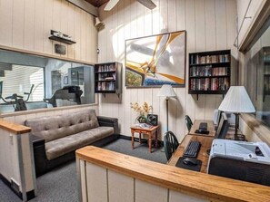 Ein gemütliches Wohnzimmer mit einer Couch, einem Couchtisch, einem Schreibtisch mit Computer und Bücherregalen.