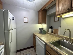 A compact kitchen with a refrigerator, dishwasher, granite countertop, sink, and wooden cabinets. - Amazing Condo 2 bedroom 2 bath with Lake Winni Views (Laconia)