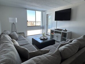 A modern living room with a sectional sofa, a coffee table, a flat-screen TV mounted on the wall, and a bookshelf. - Amazing Condo 2 bedroom 2 bath with Lake Winni Views (Laconia)