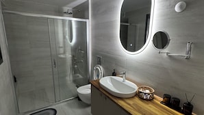A modern bathroom with a glass shower enclosure, a white sink with a wooden countertop, and a mirror with integrated lighting. - La Mer Villa Hotels (Marmaris)
