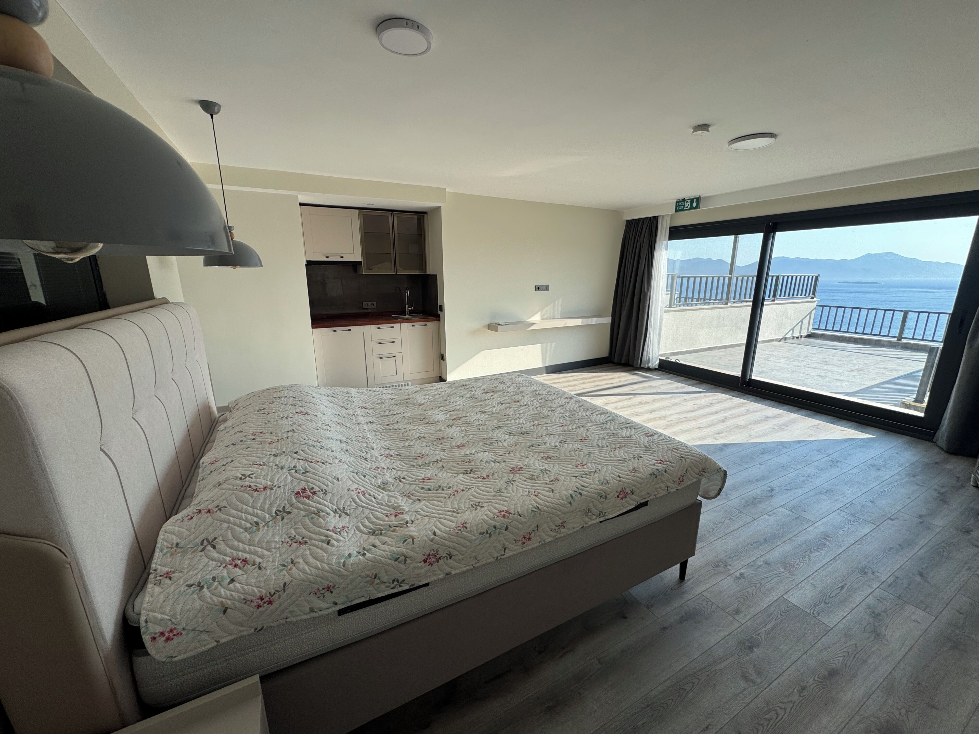 A bedroom with a large bed, a kitchenette, and a balcony with a view.