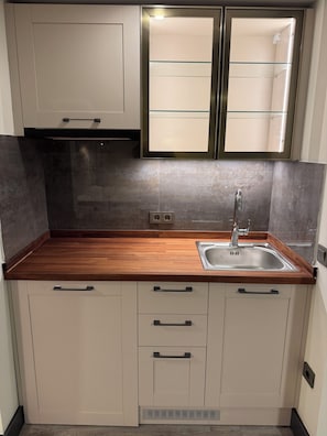 Una cocina con encimera de madera, pileta de acero inoxidable y muebles blancos.