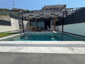 Piscina con un patio cubierto, mobiliario exterior y vista de un edificio residencial.