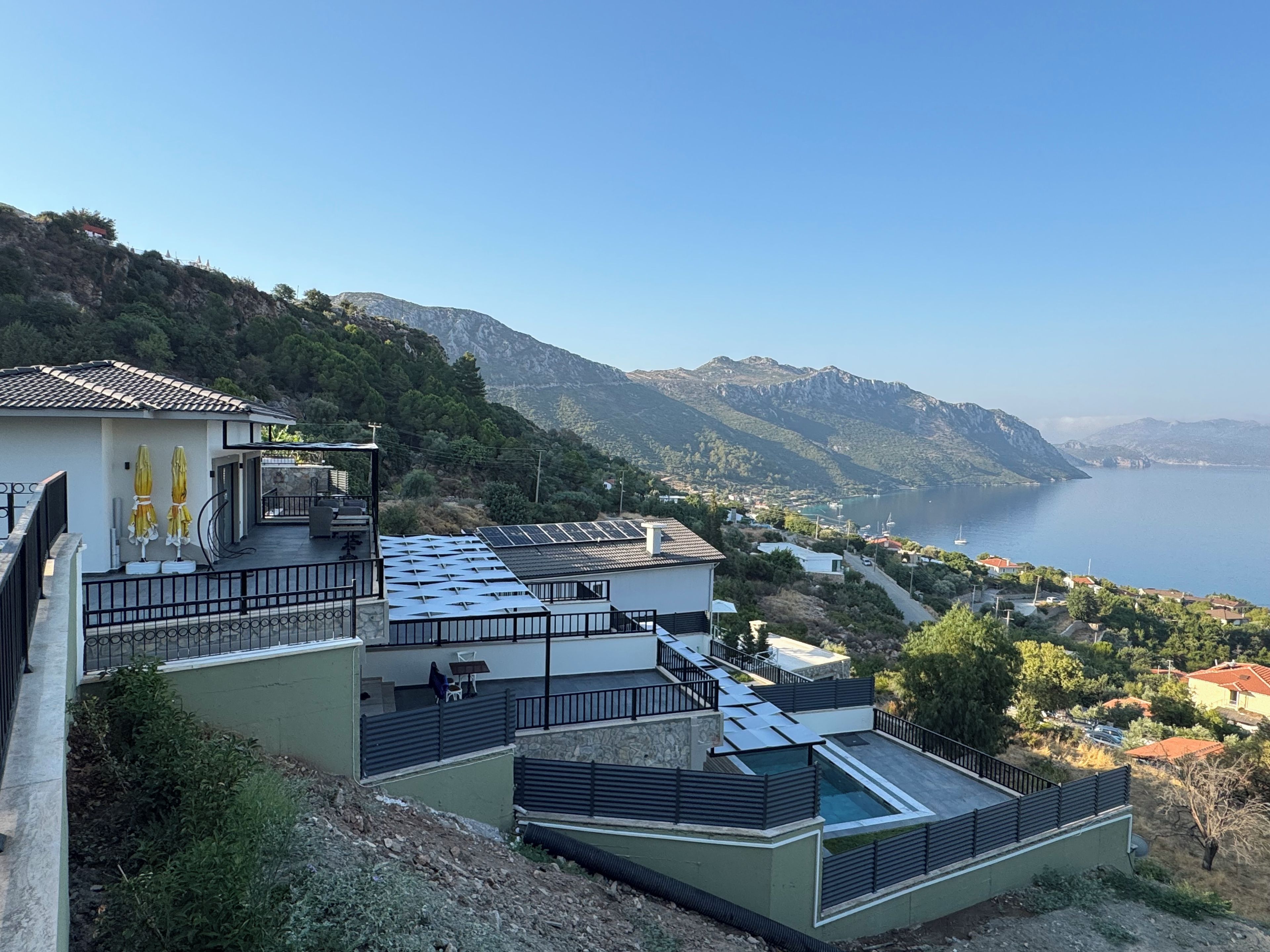 A modern building with a rooftop terrace, a view of the sea, and a mountainous backdrop.
