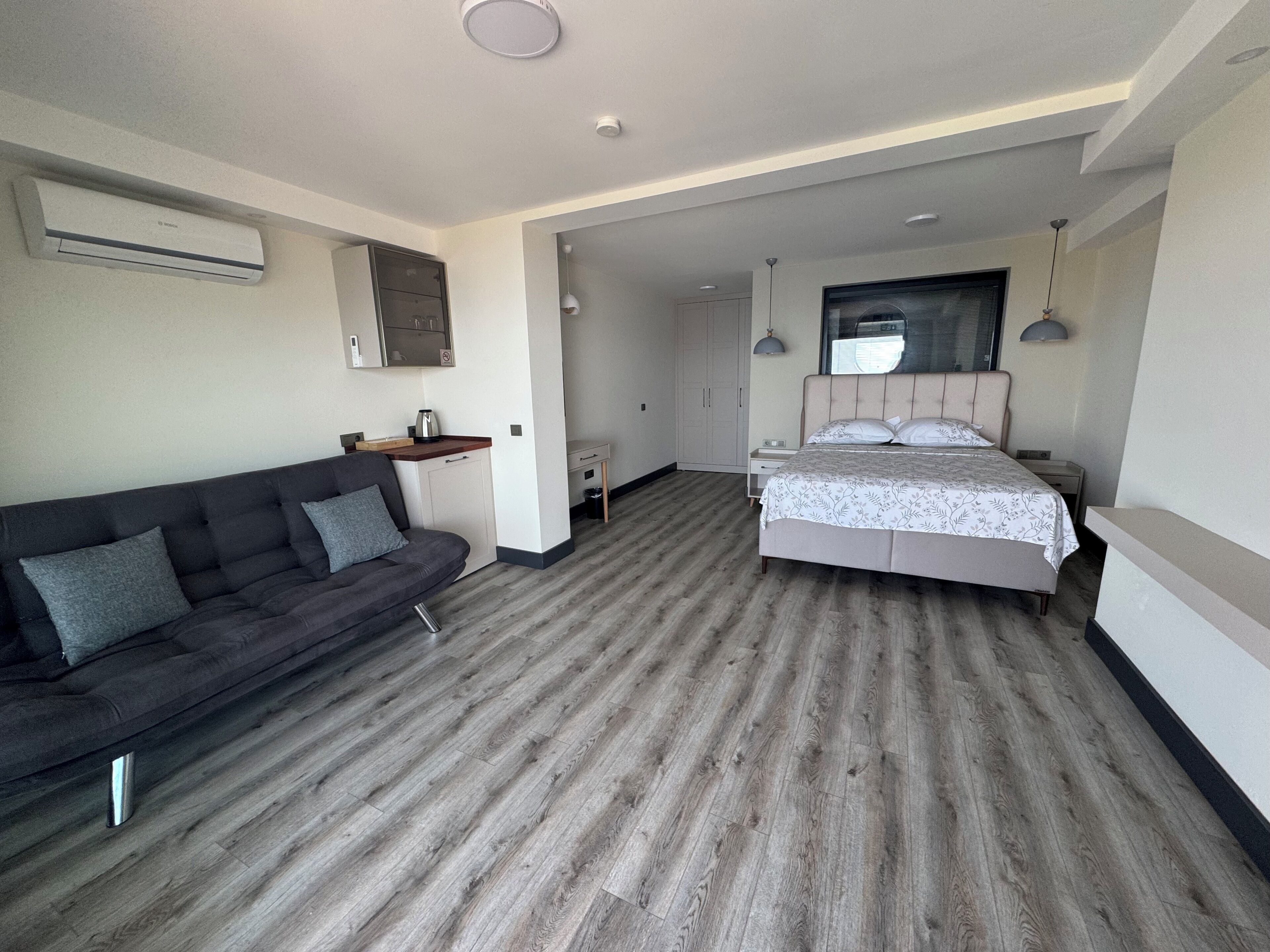 A modern hotel room with a sofa, a bed, a desk, and a wardrobe.