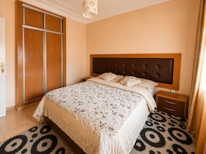 Een slaapkamer met een bed, nachtkastje, garderobe en een kamerbreed tapijt met patroon.