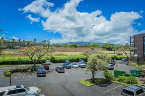 A parking lot with multiple cars, a building with a modern design, and a clear sky with clouds.