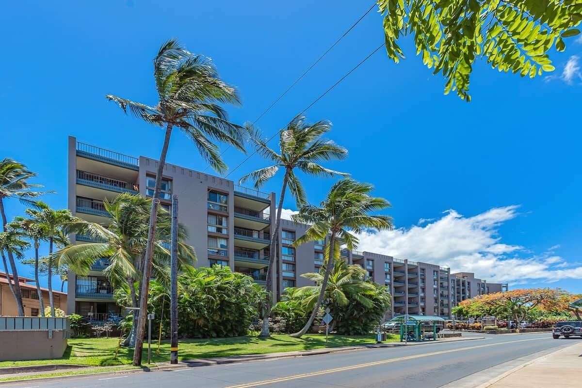 A multi-story hotel with balconies, surrounded by palm trees and a clear blue sky.