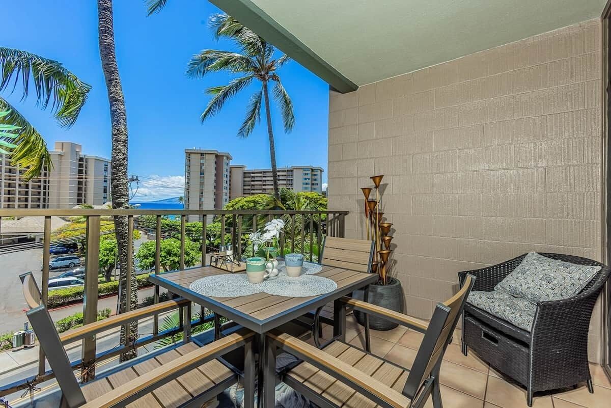 A balcony with a table, chairs, and a view of palm trees and buildings.