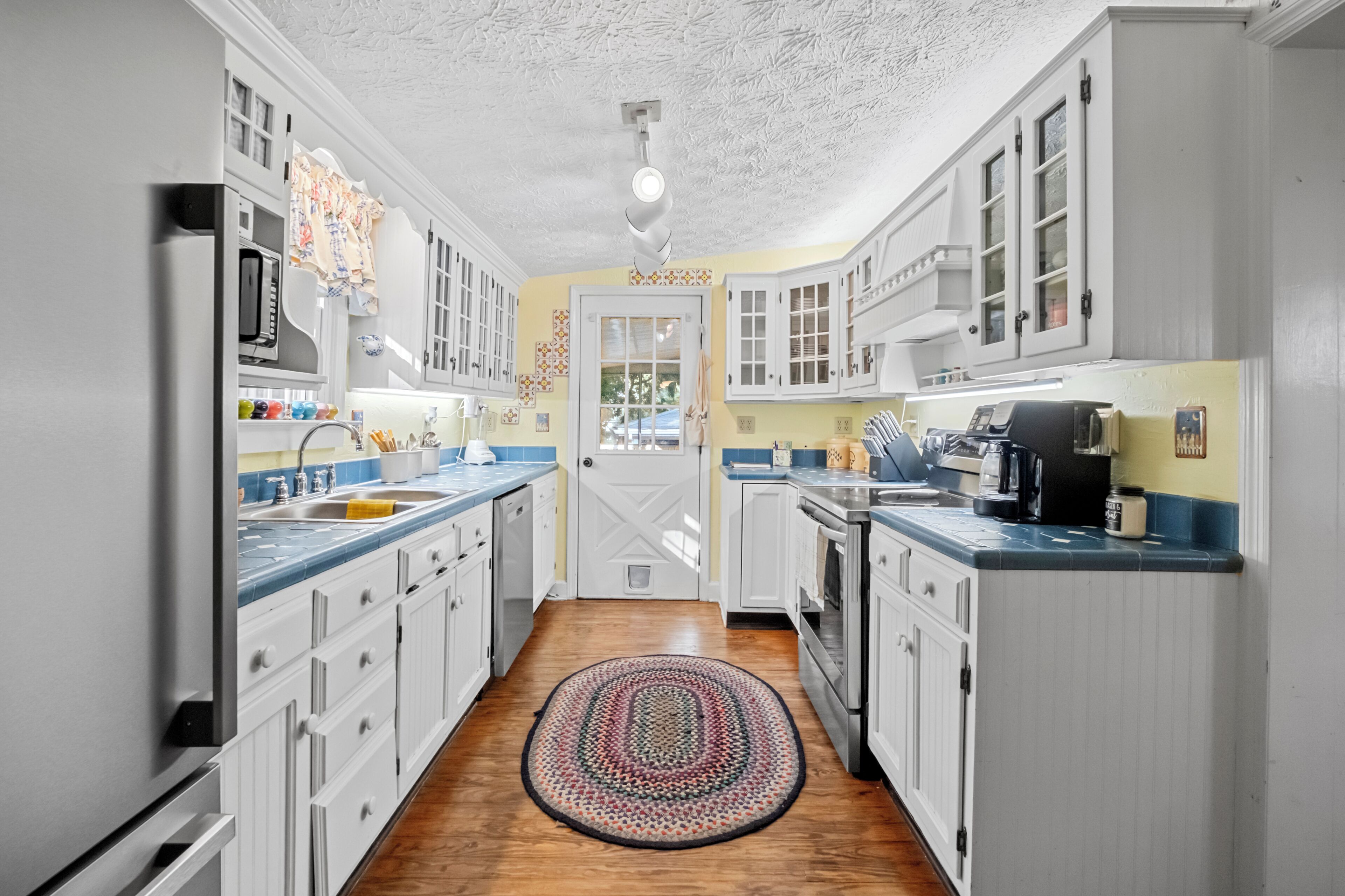 A kitchen with white cabinets, a wooden floor, and a patterned rug.