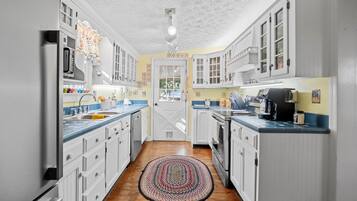 A kitchen with white cabinets, a wooden floor, and a patterned rug.