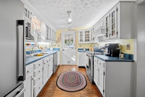 A kitchen with white cabinets, a wooden floor, and a patterned rug.
