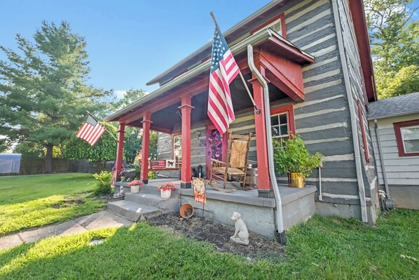 A log cabin with a porch, American flags, and a dog statue.